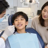 Dentist examines a boy's teeth with a dental mirror while his mother watches beside the chair. considering braces